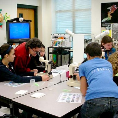 Deb Dila looking into a microscope and teaching children